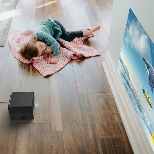 Child sleeping on wooden floor with a blanket and a projector.